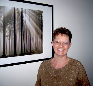 Photograph of Anne Reith standing in front of picture of woods with light shining through trees