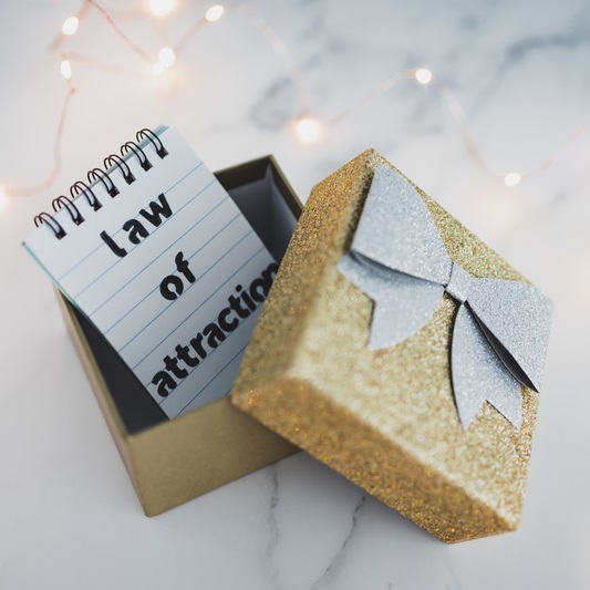 Golden gift box partially open showing a small notebook with the words Law of Attraction