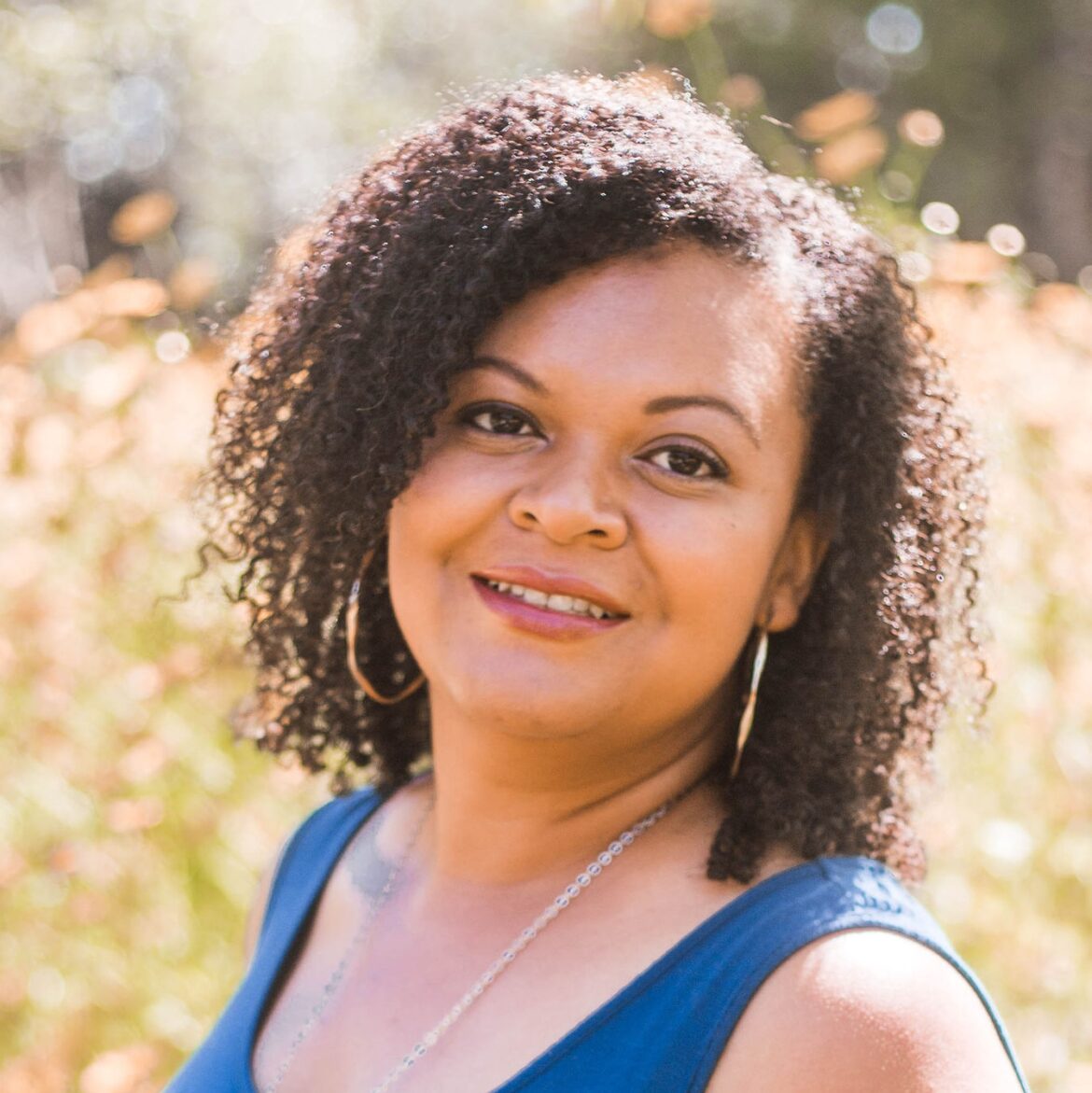 Photograph of Tanya Rillera in a blue top with a field of flowers in the background