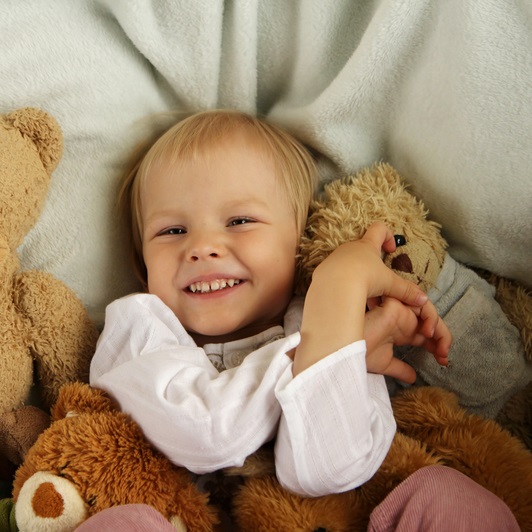 Adorable toddler in bed with arms crossed and surrounded by teddy bears