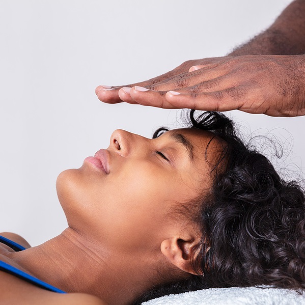 Reiki Practitioner's hands held a few inches above eyes of reclining woman in Traditional Reiki session
